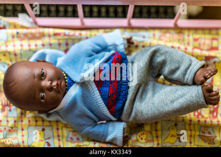 Babypuppe mit dunkler Haut, bekleidet in blauer Strickkleidung, die im Bett liegt Stockfoto