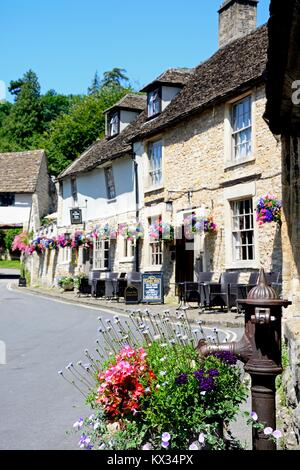 Alte Wasserpumpe und Blumen wth Das Castle Inn an der Rückseite, Castle Combe, Wiltshire, England, UK, Westeuropa. Stockfoto