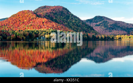 Die Hügel mit roter Ahorn Wäldern bedeckt sind in einem See in Quebec an einem schönen Herbstabend wider Stockfoto