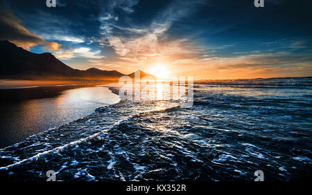 Strand Sonnenuntergang mit endlosen Horizont und einsame Figuren in der Ferne und unglaubliche schäumenden Wellen. Vulkanischen Hügel im Hintergrund Stockfoto