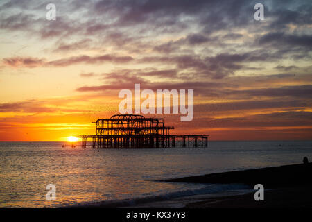 Brighton und Hove West Pier Ruinen bei Sonnenuntergang, mit der goldenen Scheibe der untergehenden Sonne Stockfoto