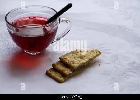 Selektiver Fokus auf transparent Tasse Hibiskus Tee auf weißen Tisch und serviert mit Cracker - Seitenansicht Stockfoto