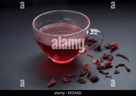 Red Hibiscus Tee in transparente Schale auf Schwarzer Tisch mit getrockneten Hibiscus Blüten dekoriert Stockfoto