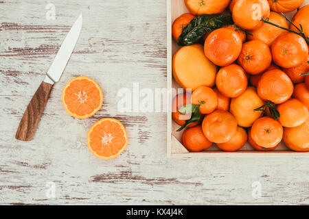 Flach mit Mandarinen in der Box, Stücke von Orange und Messer auf schäbige hölzernen Tischplatte Stockfoto