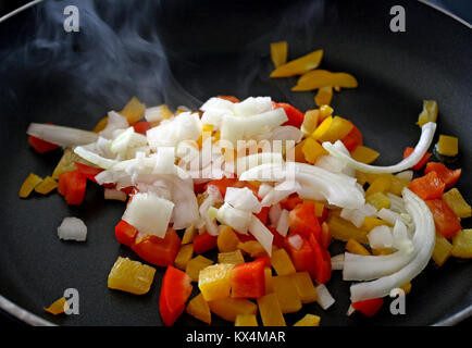 Zwiebeln mit gelben und roten Paprika braten in Pfanne Stockfoto