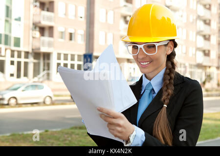 Lächelnd weibliche Ingenieur mit harten Hut lesen Blueprints, outdoor Stockfoto