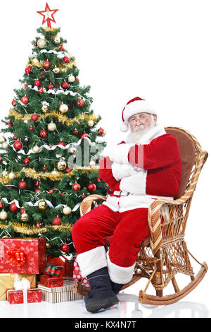 Santa Claus sitzt im Schaukelstuhl nächste volle geschmückten Weihnachtsbaum, auf weißem Hintergrund Stockfoto