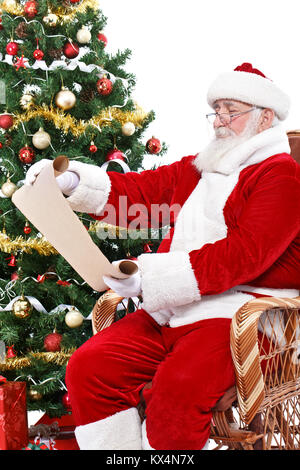 Santa Claus lesen Wunschliste, sitzt im Schaukelstuhl nächsten Weihnachtsbaum, auf weißem Hintergrund Stockfoto