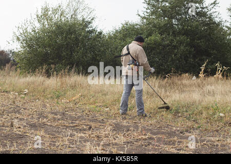 DIKANKA, UKRAINE - 30. SEPTEMBER 2015: Land Landwirt arbeiten trockenes Gras mäht Trimmer in Garten Stockfoto