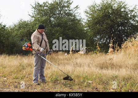 DIKANKA, UKRAINE - 30. SEPTEMBER 2015: Land Landwirt arbeiten trockenes Gras mäht Trimmer in Garten Stockfoto