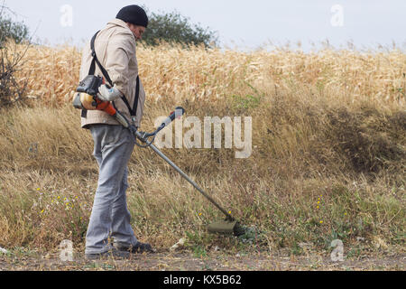 DIKANKA, UKRAINE - 30. SEPTEMBER 2015: Land Landwirt arbeiten trockenes Gras mäht Trimmer in Garten Nahaufnahme Stockfoto