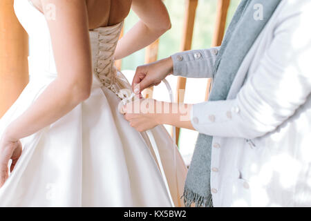 Familie, Hochzeit, Beziehungen Konzept. fürsorgliche Mutter hilft, Ihre anmutige Tochter für wichtige Vorbereitung und Dressing ihre strahlend weißen Kleid der Braut. Stockfoto