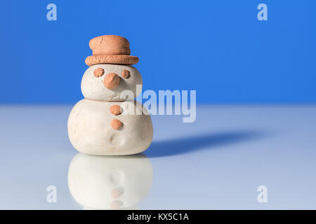 Kleine Figur eines Schneemannes mit einem braunen Hut, blauer Hintergrund Stockfoto