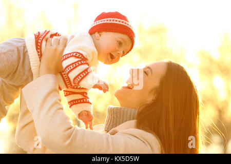 Hintergrundbeleuchtung Porträt einer fröhlichen Mutter ihr Baby im Freien, bei Sonnenuntergang im Winter Stockfoto