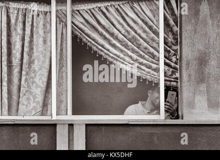 Mann mit Handy, Fenster in Hochhaus in Spanien. Stockfoto