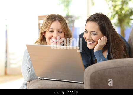 Zwei glückliche Mitbewohner beobachten auf Inhalte in einem Laptop auf einer Couch im Wohnzimmer zu Hause liegen Stockfoto