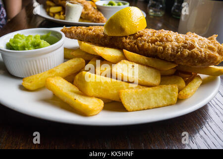 Traditionelle iconic Britische Fisch und Chips mit Erbsenpüree in einem typischen englischen Public House serviert. Stockfoto