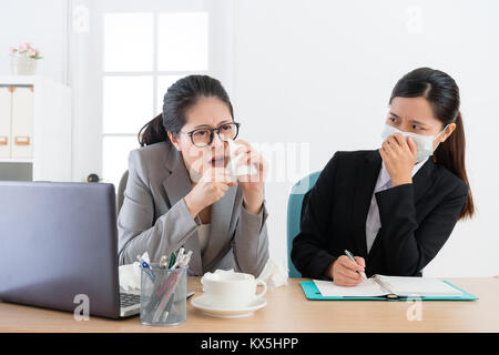 Junge hübsche Geschäftsfrau mit medizinischen Maske Gefühl Furcht, wenn Office Manager der Arbeitnehmer bei Krankheit und während der Sitzung Zeit Husten. Stockfoto