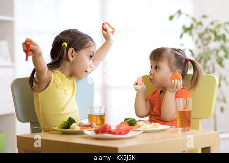 Süß lächelnd Kind und Kind Kleinkind Mädchen spielen und essen Spaghetti mit Gemüse für gesundes Mittagessen sitzen in einem weißen sonnige Küche mit großem Wind Stockfoto