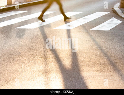 Blurry Beine und Schatten eines Jugendmädchen überqueren Sie die kleine Straße der Stadt bei Sonnenuntergang in Eile Stockfoto