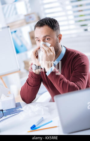 Junge kranker Mann drücken eine Serviette auf seinem Gesicht, während seine Nase weht Stockfoto