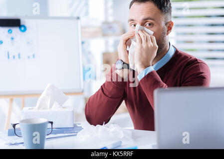 Junger Mann auf der Suche nachdenklich, während seine Nase bei der Arbeit weht Stockfoto