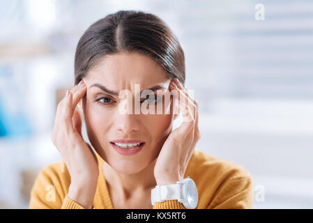 Junge Frau runzelte die Stirn, während sie an einer sehr schmerzhaften Migräne Stockfoto