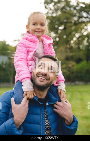 Süße kleine Mädchen reiten auf Vater zurück in den Park Stockfoto