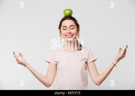 Porträt einer recht entspannt Mädchen meditieren mit einem Apfel auf dem Kopf auf weißem Hintergrund Stockfoto