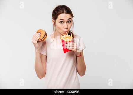 Nahaufnahme, Porträt einer jungen hübschen Mädchen Essen Pommes und Burger auf weißem Hintergrund Stockfoto