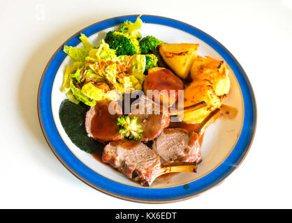 Englisch Abendessen Braten Lammkarree Brokkoli cabbage Roast Potatoes mint Sauce, Soße, serviert auf einem blauen und weißen Platte auf weißem Hintergrund Stockfoto