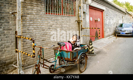 Ein junges Mädchen sitzt auf einem Fahrrad Warenkorb in den reservierten Parkplatz an ihrem Wohnsitz. Traditionelle houton Bereich. Peking, China Stockfoto