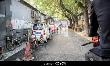 Eine Gasse in einem traditionellen Chinesischen houton Bereich mit Autos, Fahrräder und Menschen. Peking, China Stockfoto