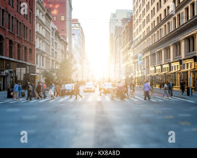 Masse der anonymen Menschen überqueren die Straße an einer belebten Kreuzung in Manhattan, New York City mit den hellen Schein der Sonnenuntergang im Hintergrund Stockfoto