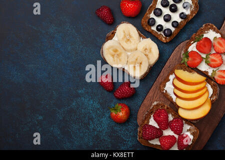 Diät Frühstück. Toast mit Frischkäse und frischen Beeren und Früchte: Bananen, Himbeere, Heidelbeere, Erdbeere, Pfirsich. Stockfoto