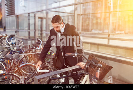 Young Business Mann mit Kopfhörer setzt Fahrrad Fahrradständer in der Stadt Stockfoto