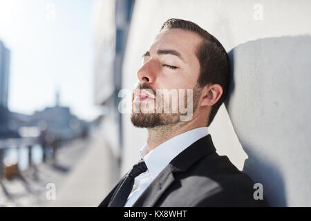 Unternehmer lehnt sich gegen eine Wand in der Sonne und entspannende Stockfoto
