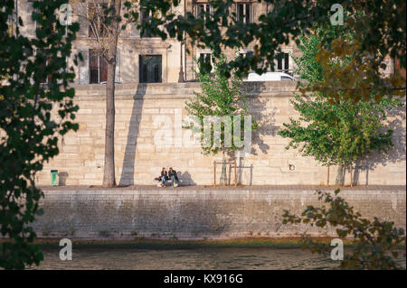 Junge Menschen vielfältiges Paris, Blick auf ein Paar, das zusammen in der Sonne am Quai d'Orleans auf der Ile St Louis im Zentrum von Paris sitzt. Stockfoto