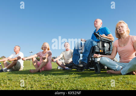 Behinderte Menschen mit einer Gruppe von Menschen üben Yoga außerhalb. Stockfoto