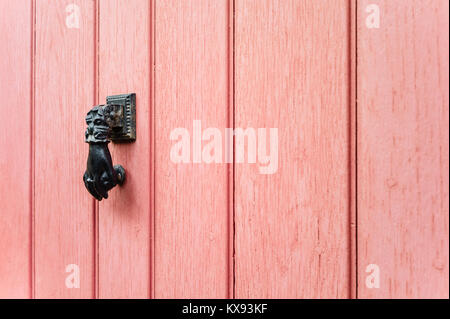 Seitenansicht eines schwarzen Hand-förmigen Tür-Klopfer auf einem alten Pink vordere Tür ausgestattet. Stockfoto