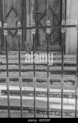 Nahaufnahme einer dekorativen Iron Gate, mit Steintreppen und alte hölzerne Flügeltüren im Hintergrund, in Schwarz und Weiß, in Guanajuato, Mexiko Stockfoto