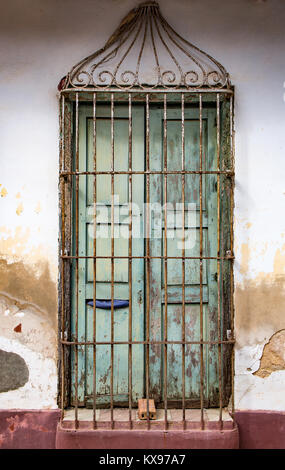Verblasste grüne Tür mit Vorhängeschloss hinter Metall Gitter auf befleckt weiße Wand in Trinidad, Kuba Stockfoto