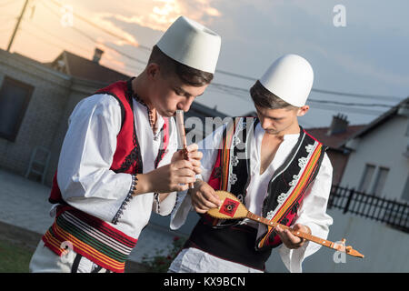 Jugendlich Jungen in der traditionellen albanischen Kostüm spielen Musik mit Flöte und String Instrument in der Abendsonne Stockfoto