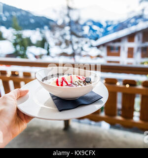 Blaubeere, Banane und Maca Smoothie Schüssel mit Chia Samen, Sonnenblumenkerne und Kokosnuss. Gesundes Frühstück mit schönem Blick auf die Berge in Verbier, Swis Stockfoto