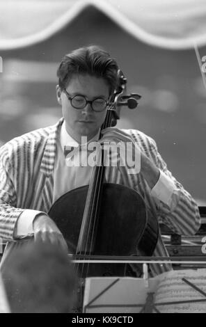 Juli 1990, Henley on Thames, Oxfordshire, England. Henley Royal Regatta Szene auf der Themse. Ein cellist sorgt für die Atmosphäre Foto von Tony Henshaw Stockfoto