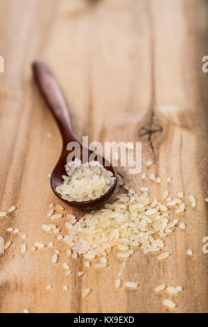 Rohen Langkornreis gedämpftem Reis in einem Löffel auf einer hölzernen Hintergrund. Zutaten für eine gesunde Ernährung. Stockfoto