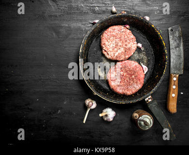 Raw-Burger aus Rindfleisch in eine alte Pfanne mit Knoblauch und Gewürzen. Auf der schwarzen Tafel. Stockfoto