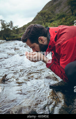 Männliche wanderung Trinkwasser aus dem Stream Stockfoto