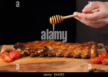 Cooking Pork Rib Koteletts mit Honig süßen Soße auf dunklem Hintergrund. Der Küchenchef gießt Honig Rippchen. Mit kopieren. Stockfoto