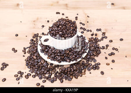 Viele Kaffeebohnen auf hölzernen Hintergrund und weiße Tasse Stockfoto